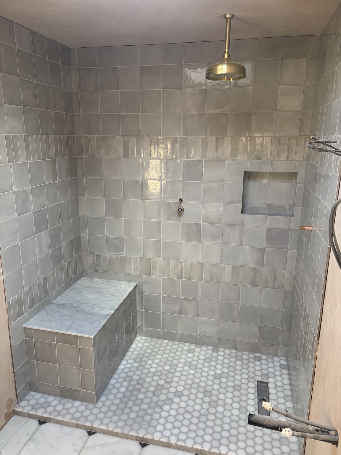 Grey tiled wet room with a marble mosaic wet tray, tiled seat and niche